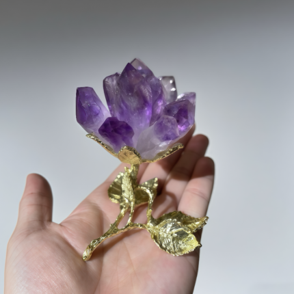 Amethyst crystal lotus flower with gold - plated stem and leaves held in a hand