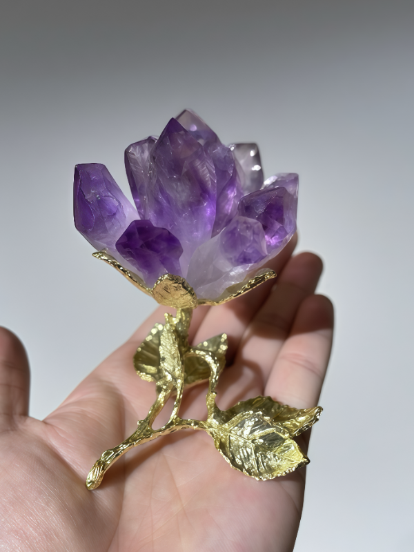Amethyst crystal lotus flower with gold - plated stem and leaves held in a hand