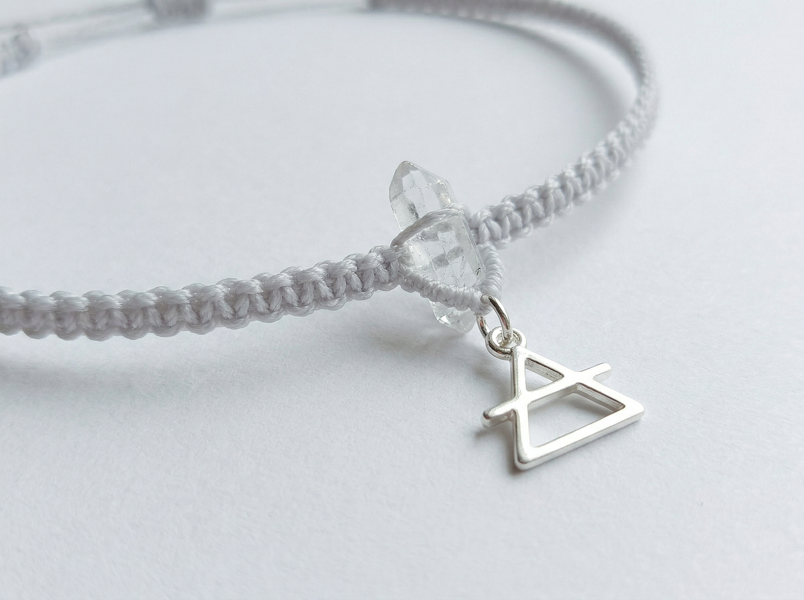 Air sign minimalist choker featuring a clear quartz point, pale grey cord, and a shiny silver zodiac charm.
