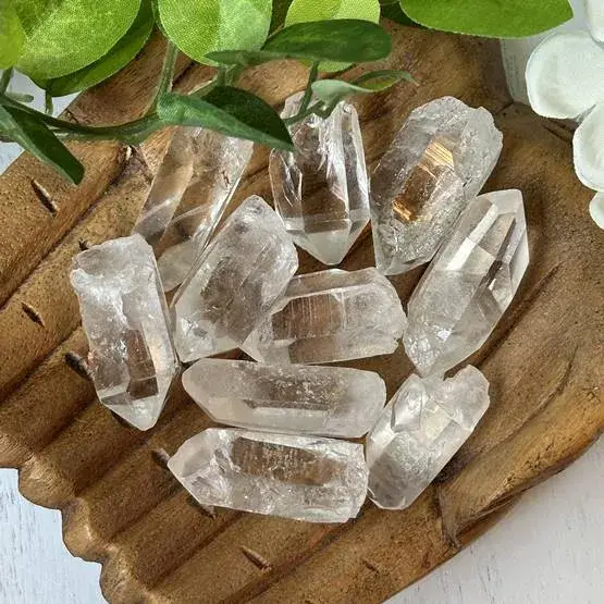 Cluster of natural clear quartz points on a wooden table under soft daylight, showing raw crystal textures.