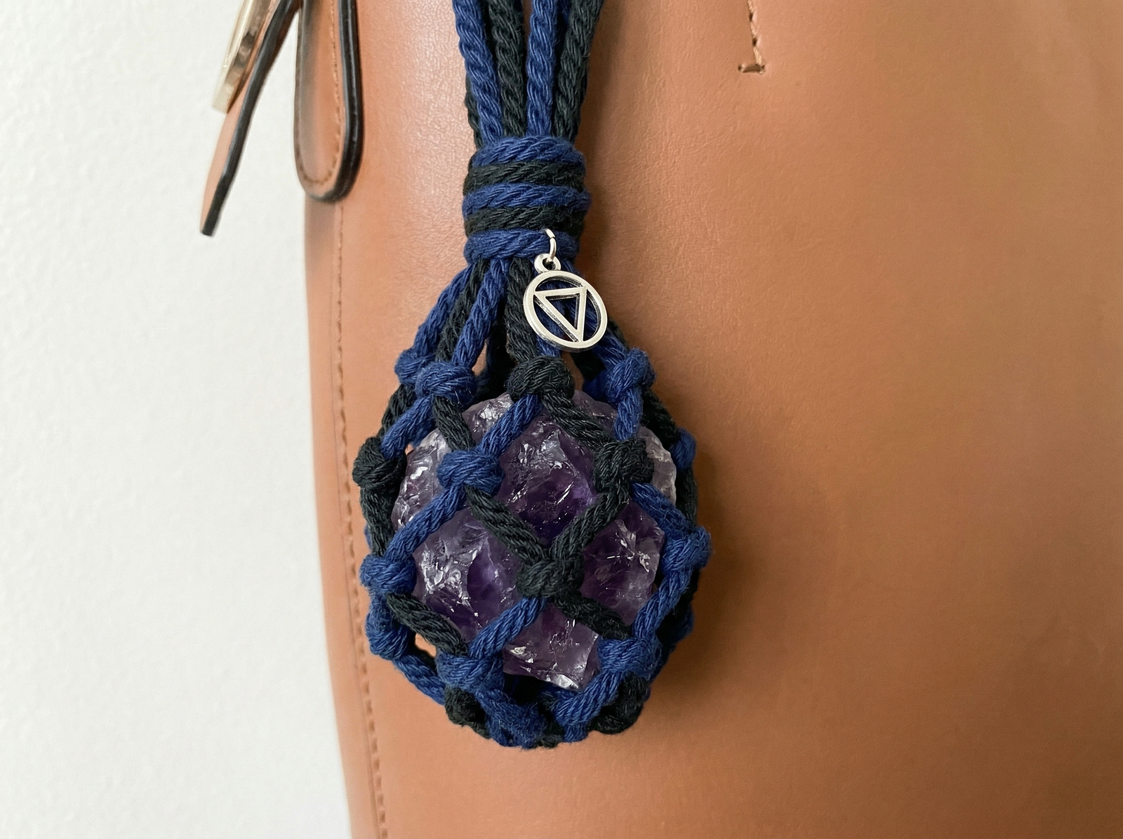 Water sign protective amulet featuring a raw amethyst enclosed in a navy blue macrame net with a silver charm.