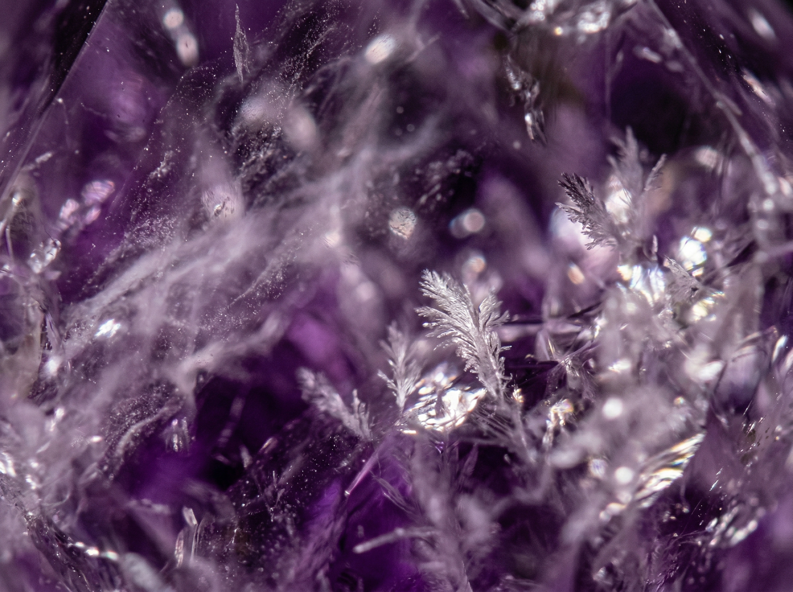 Macro shot of real amethyst showing natural internal mists and feather inclusions without any artificial air bubbles.